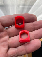 Dos soportes impresos en 3D de color rojo para tuerca M8, sostenidos en una mano.