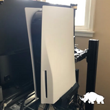 PlayStation 5 colocada de forma ordenada en un soporte detrás de un monitor, asegurando estabilidad y un diseño limpio en el espacio.